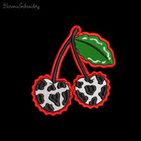 Two cherries with cow print texture and green leaves, finished with a wavy red border embroidery design.