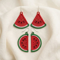 Two mirrored FSL watermelon slice earrings — a machine embroidery design in Free Standing Lace technique, showing red lace fill, black seeds, and green border with a hanging loop.