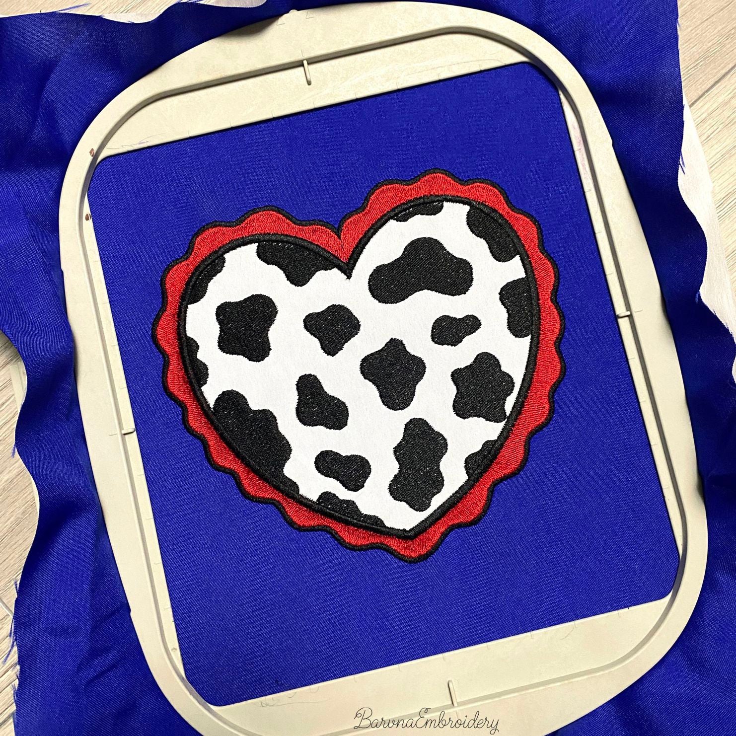 Machine embroidery design showing two versions of a cow print heart: one small filled and one large applique with a red wavy border.