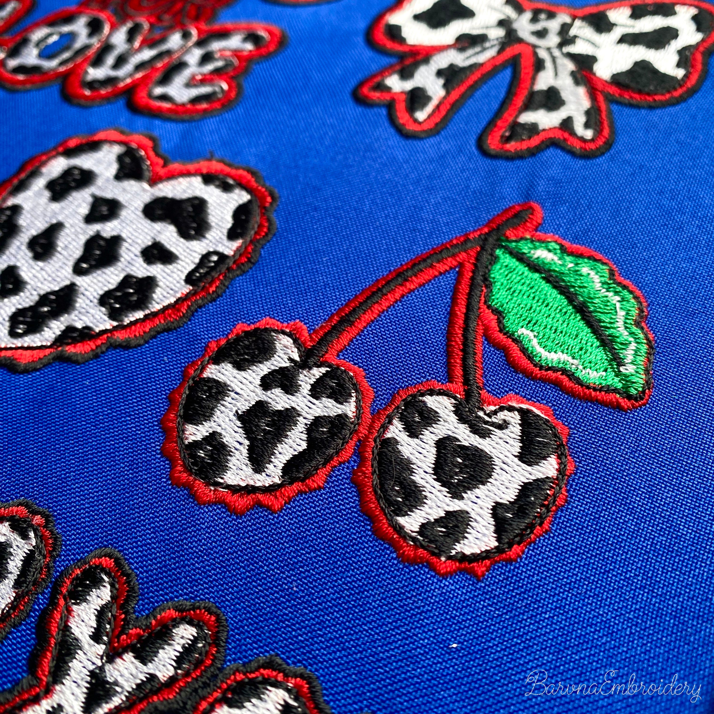 Two cherries with cow print texture and green leaves, finished with a wavy red border embroidery design.