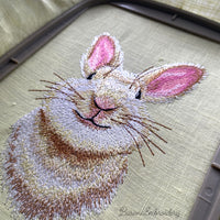 Detailed machine embroidery design of a cute smiling bunny head with prominent pink ears, realistic brown and white fur textures, and long whiskers.