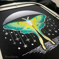 Green luna moth machine embroidery design positioned beneath crescent moon with stars