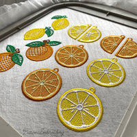 Three pairs of FSL lemon embroidery earrings — half-slice, whole lemon with green leaves, and round citrus slice — displayed on cream fabric, Free Standing Lace machine embroidery design.