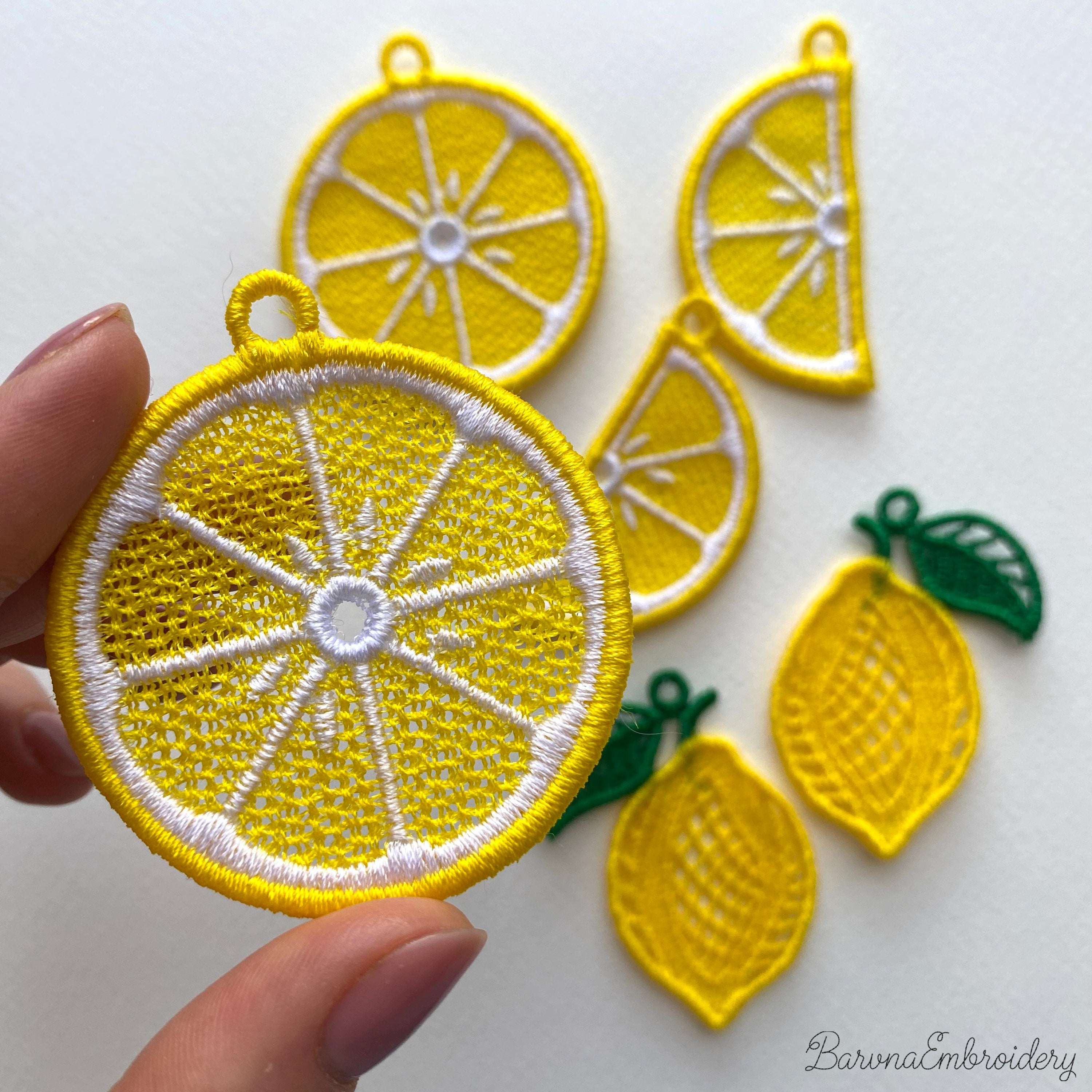 Three pairs of FSL lemon embroidery earrings — half-slice, whole lemon with green leaves, and round citrus slice — displayed on cream fabric, Free Standing Lace machine embroidery design.