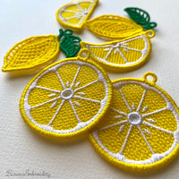 Three pairs of FSL lemon embroidery earrings — half-slice, whole lemon with green leaves, and round citrus slice — displayed on cream fabric, Free Standing Lace machine embroidery design.