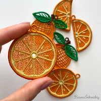 Three pairs of FSL orange embroidery designs — half-slice, whole orange with green leaves, and round citrus cross-section — Free Standing Lace machine embroidery pattern for earrings and pendants.