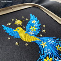 Blue and yellow flying bird embroidery design with stars and flowers trailing from wings – symbolic Ukrainian patriotic motif.