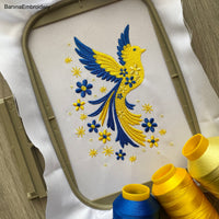 Blue and yellow flying bird embroidery design with stars and flowers trailing from wings – symbolic Ukrainian patriotic motif.