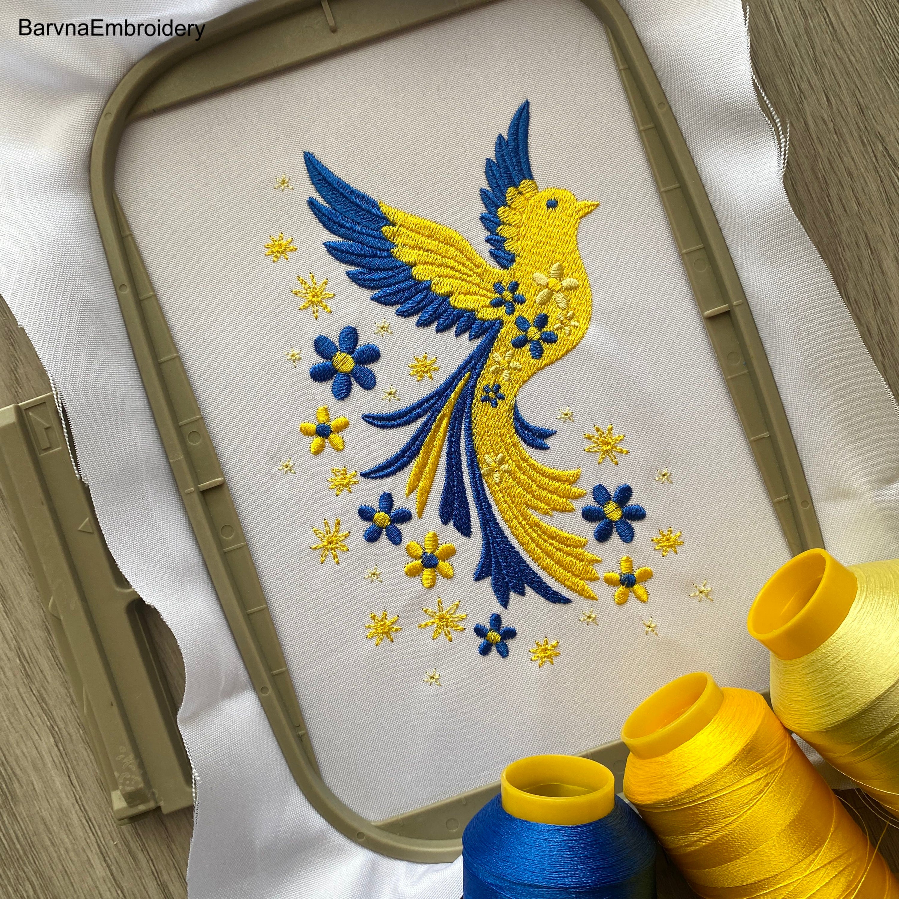 Blue and yellow flying bird embroidery design with stars and flowers trailing from wings – symbolic Ukrainian patriotic motif.