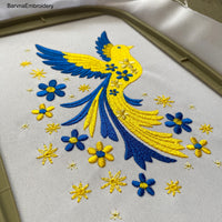 Blue and yellow flying bird embroidery design with stars and flowers trailing from wings – symbolic Ukrainian patriotic motif.
