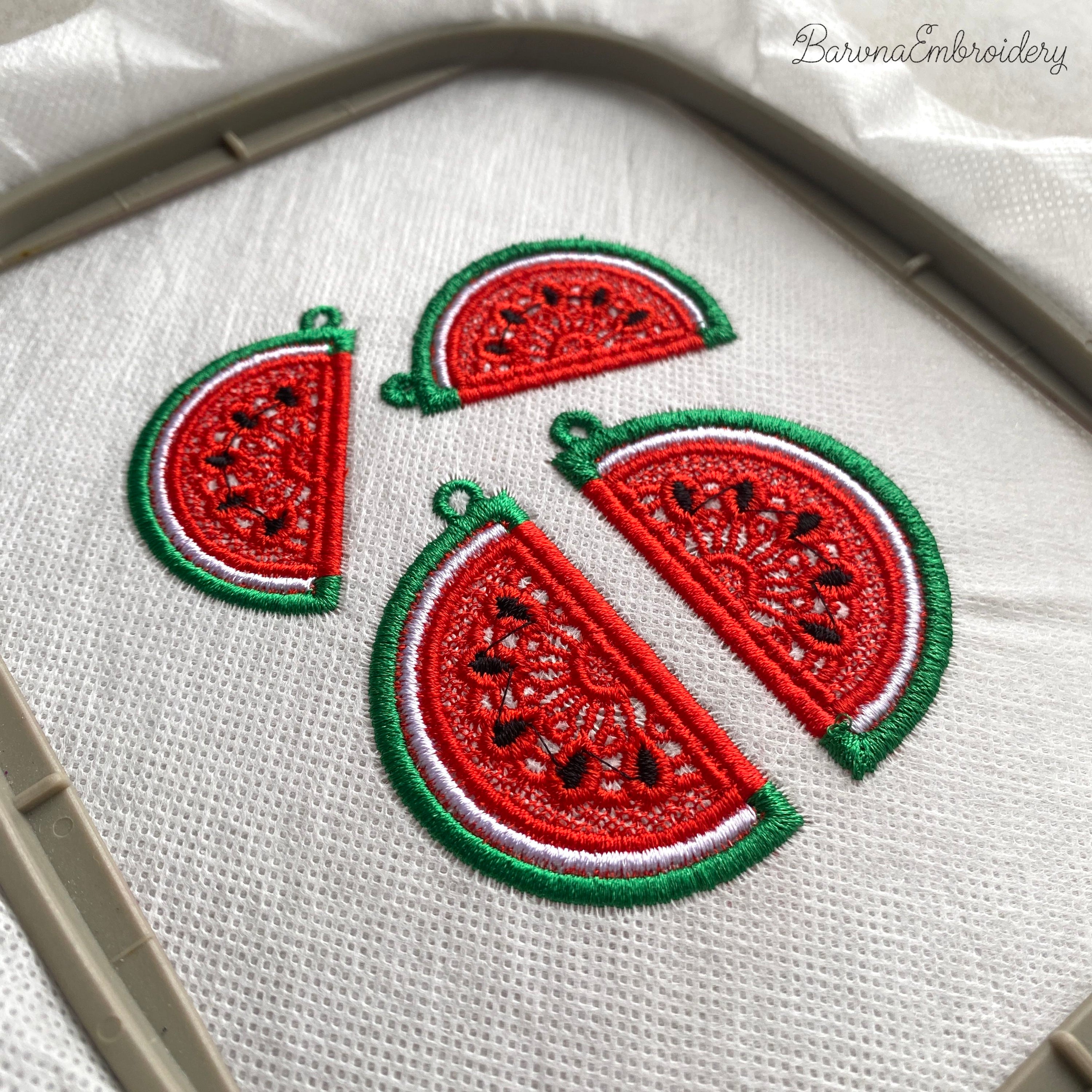 Two mirrored FSL watermelon slice earrings — a machine embroidery design in Free Standing Lace technique, showing red lace fill, black seeds, and green border with a hanging loop.