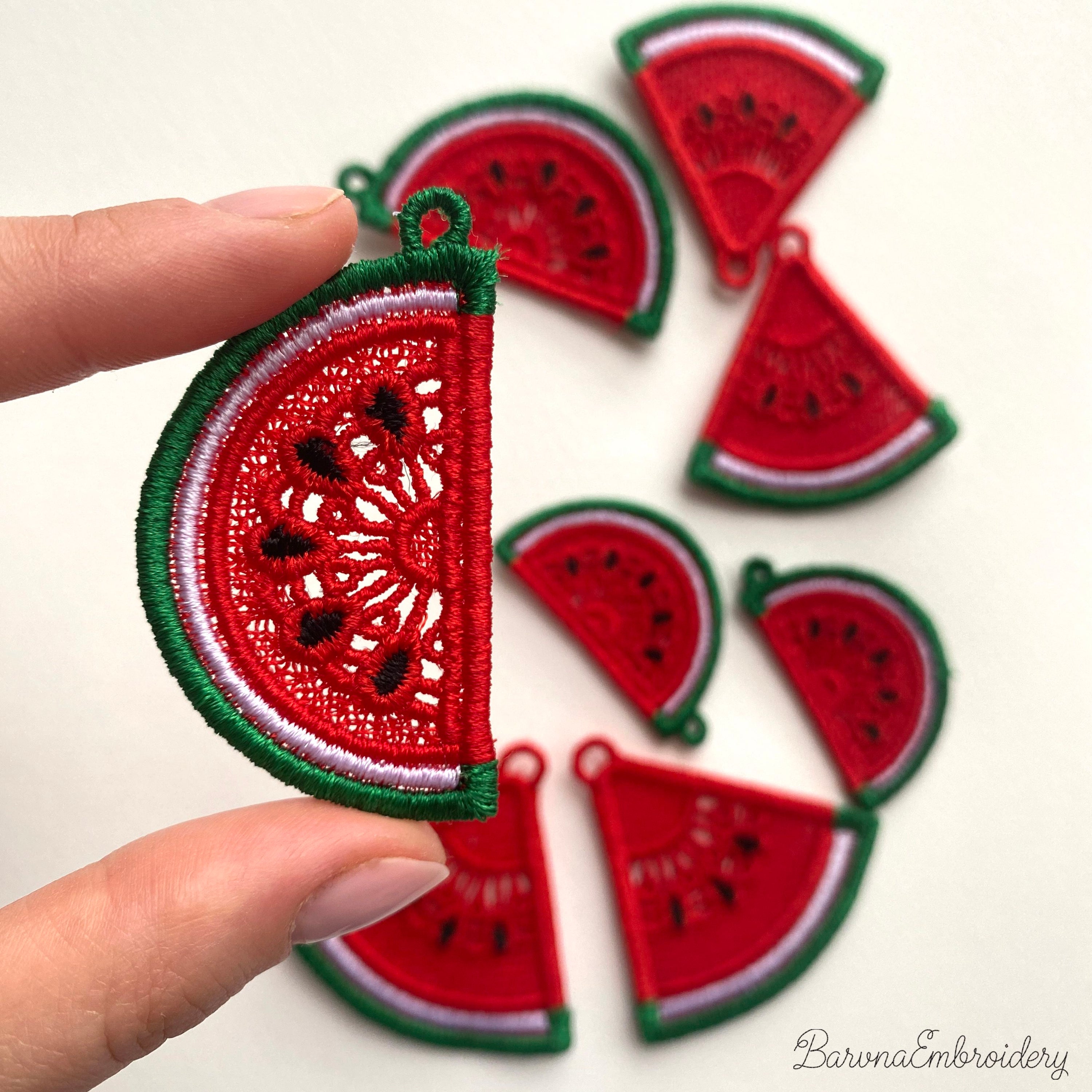 Two mirrored FSL watermelon slice earrings — a machine embroidery design in Free Standing Lace technique, showing red lace fill, black seeds, and green border with a hanging loop.