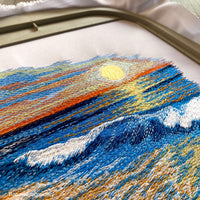 Machine embroidery design of a seaside landscape with golden sand, gentle ocean waves, and a vibrant sunset.