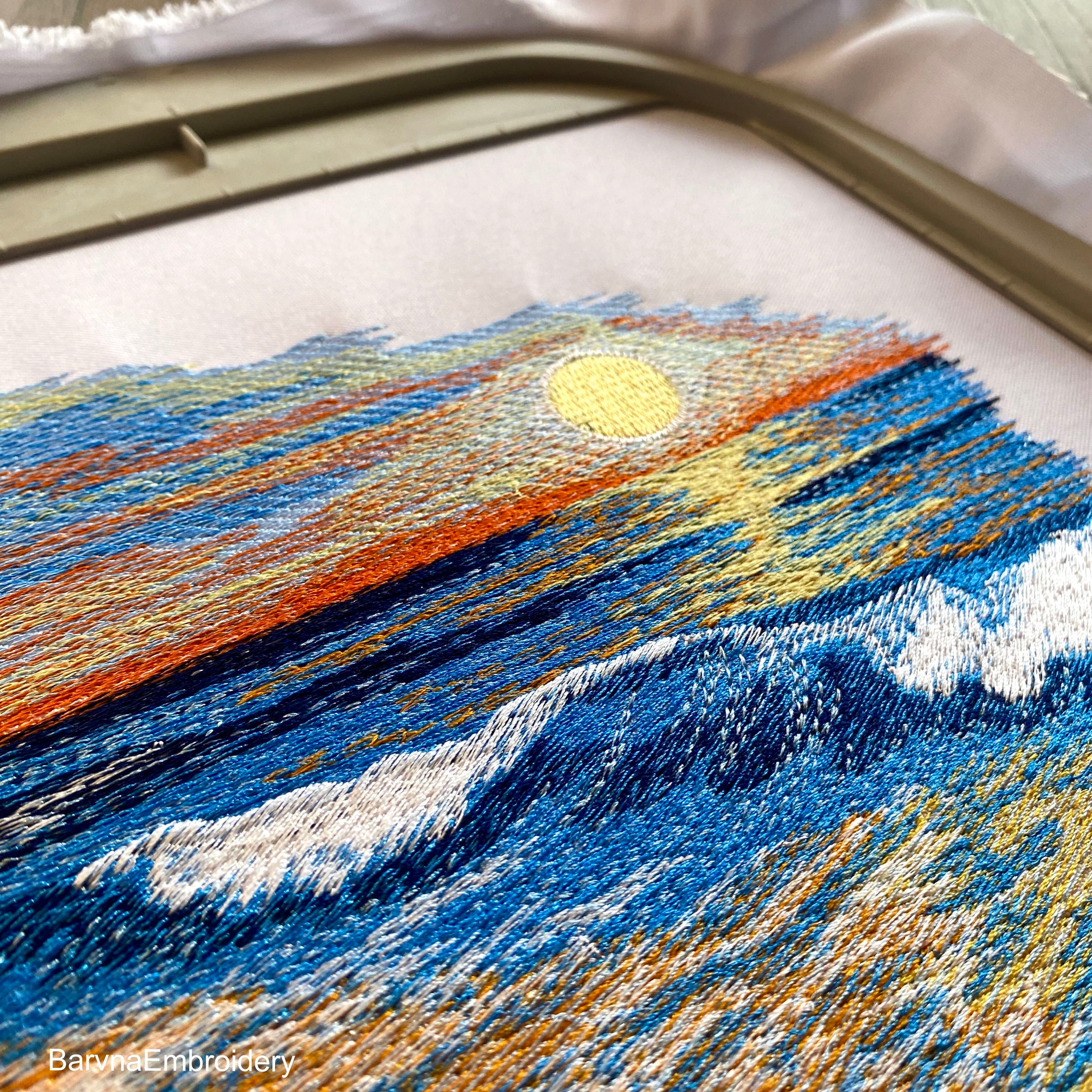 Machine embroidery design of a seaside landscape with golden sand, gentle ocean waves, and a vibrant sunset.