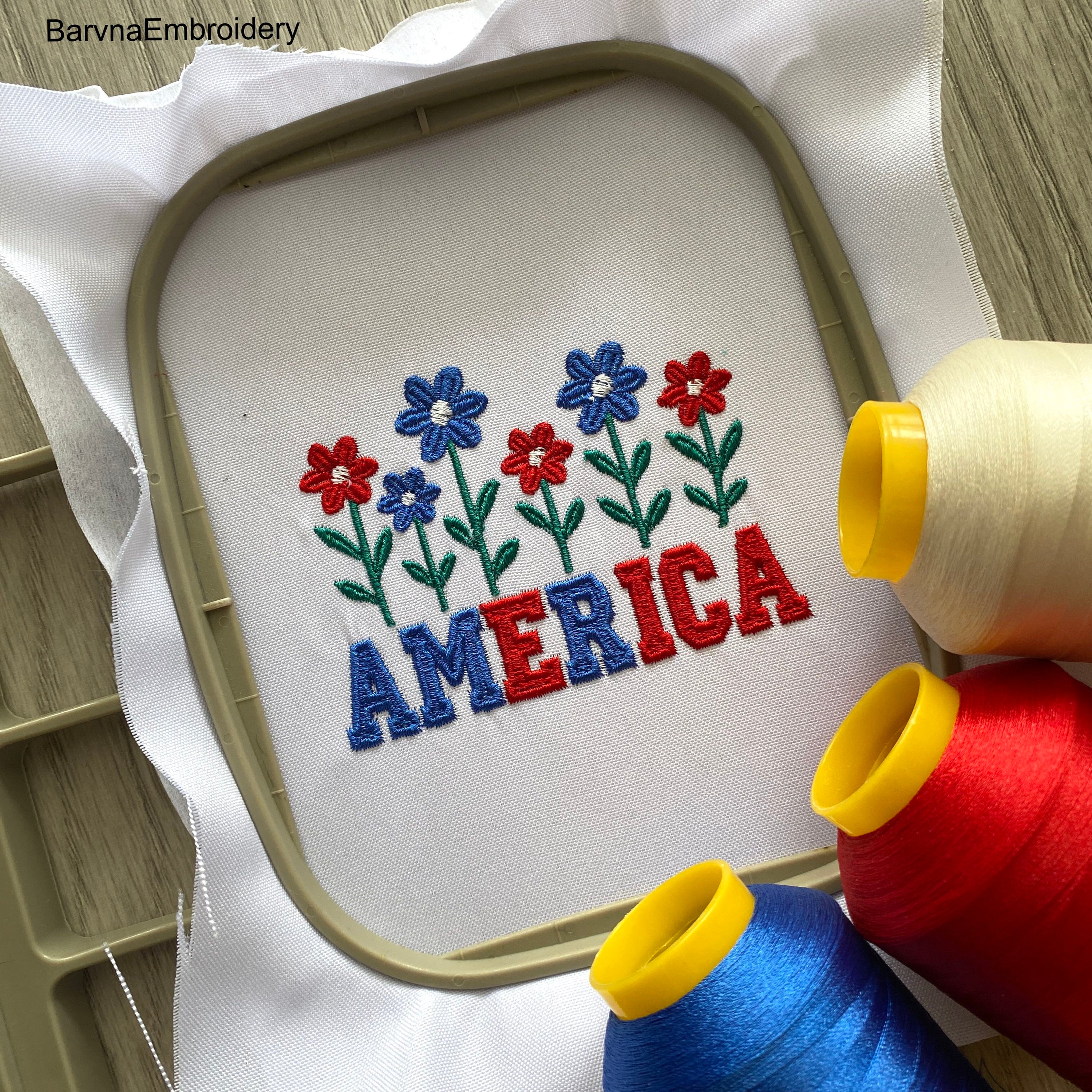 Machine embroidery design of the word “America” decorated with red, white, and blue flowers, perfect for patriotic crafts and 4th of July projects.