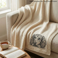 Black and white embroidered illustration of a long-haired dachshund dog. The dog is lying down, with its paws and head resting on a surface. The dog's eyes are open, and it has long, flowing fur.