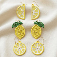 Three pairs of FSL lemon embroidery earrings — half-slice, whole lemon with green leaves, and round citrus slice — displayed on cream fabric, Free Standing Lace machine embroidery design.