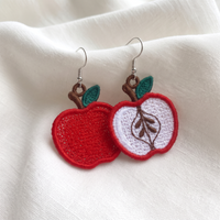 Whole red apple and sliced apple FSL earring designs displayed as finished lace pieces on soft white fabric
