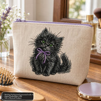 Cream cosmetic bag mockup with black kitten embroidery, a purple bow and a lavender zipper on a wooden vanity.
