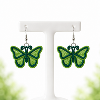 Green butterfly FSL earrings with lace-filled wings and silver hooks hanging on a white jewelry stand