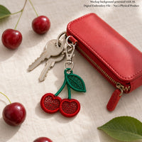 Red cherry FSL keychain attached to silver keys beside a red wallet and fresh cherries