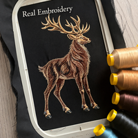 Actual stag embroidery on black fabric in a hoop, with open areas between the fur stitches and thread spools beside it.
