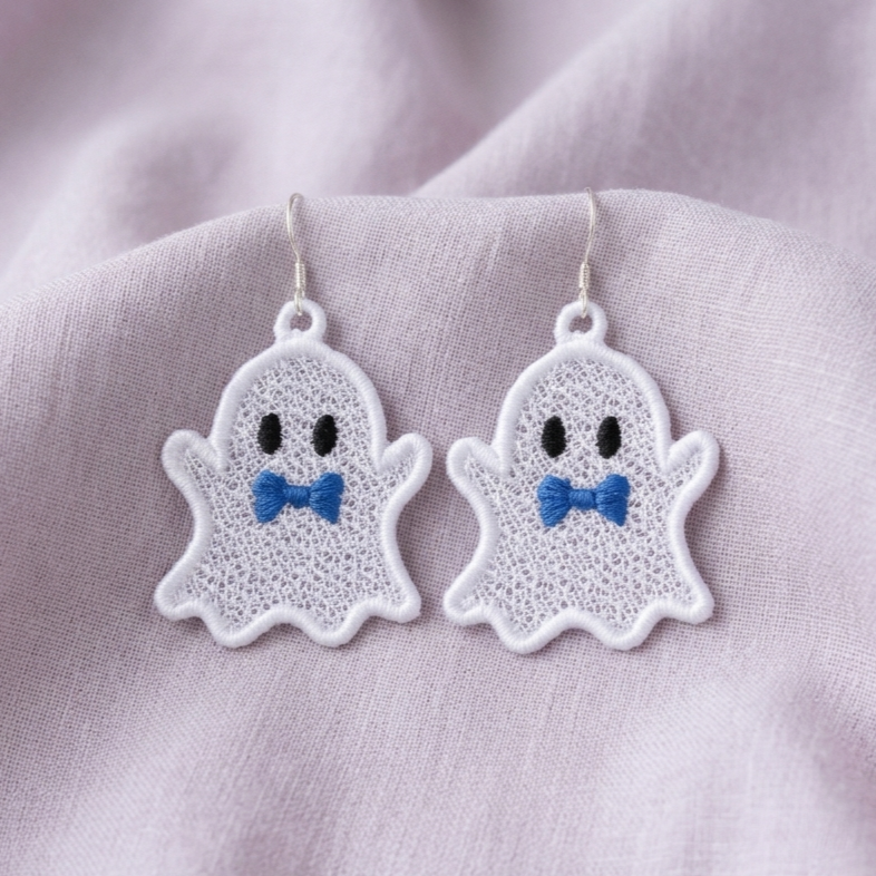 Pair of white Ghost Boy FSL earrings with blue bow ties, black oval eyes and silver hooks on lavender fabric