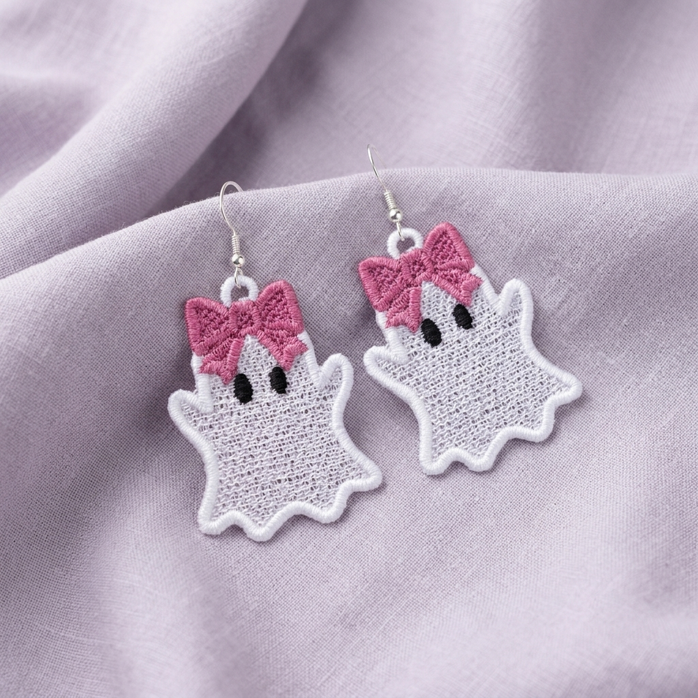 Pair of white Ghost Girl FSL earrings with large pink bows, black eyes and silver hooks on lavender fabric