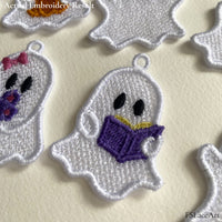 Close-up of an embroidered reading ghost with a purple book, showing the white lace texture, satin border and hanging loop.