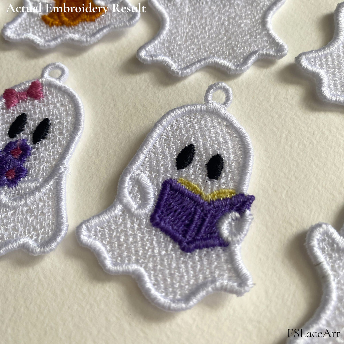 Close-up of an embroidered reading ghost with a purple book, showing the white lace texture, satin border and hanging loop.