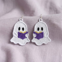 White lace ghost earrings holding open purple books, displayed on soft lavender fabric with silver hooks.