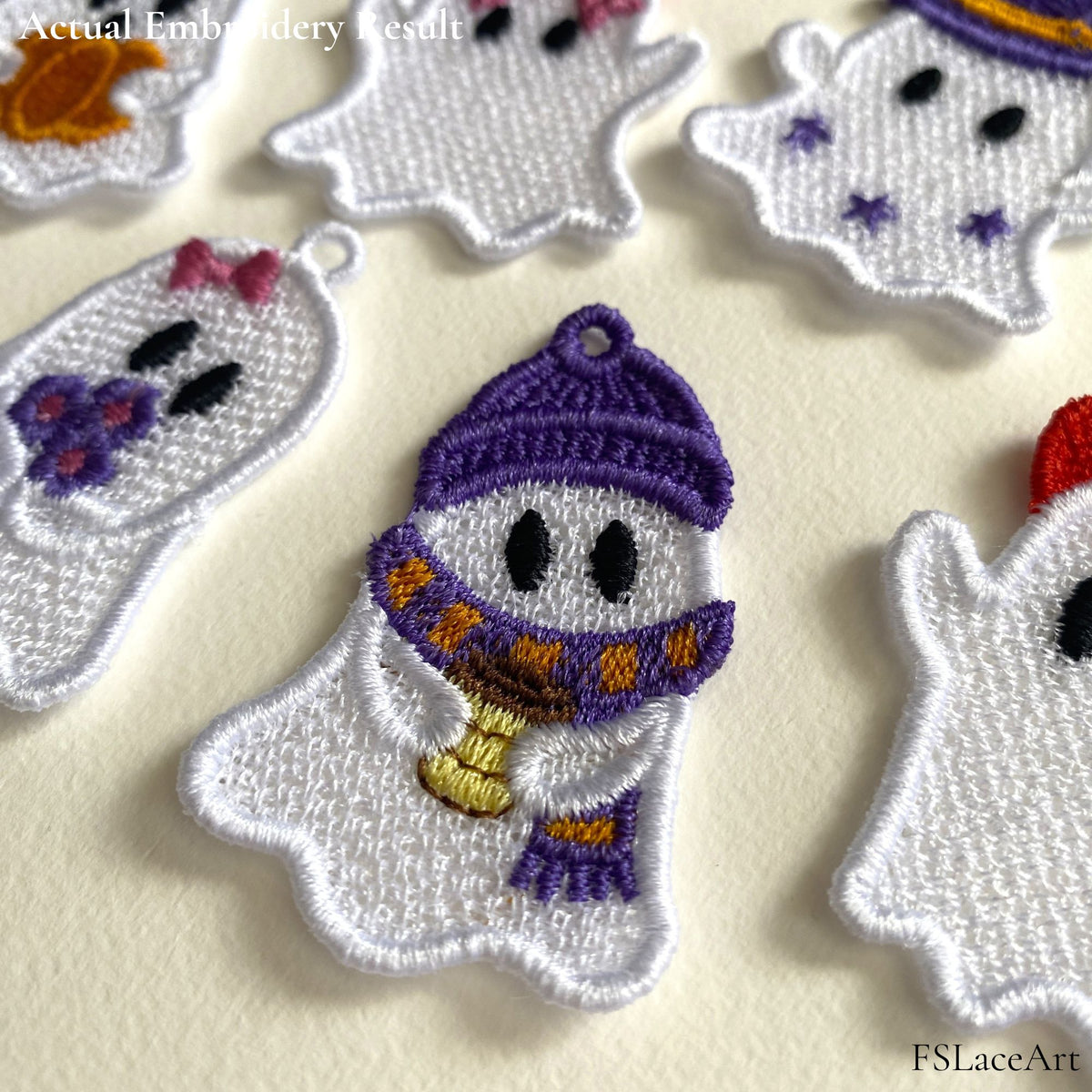 Close-up of an embroidered lace ghost holding a coffee cup, with a purple hat, striped scarf and hanging loop.