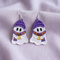 White ghost earrings with purple hats and scarves, holding coffee cups, displayed on soft lavender fabric.