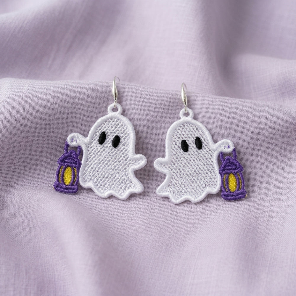 Pair of white ghost FSL earrings holding purple lanterns with yellow centers on soft lavender fabric