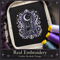 Actual gothic keyhole embroidery on black fabric in a hoop beside white, purple and blue-gray thread spools.