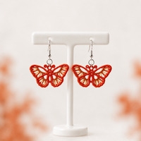 Pair of orange Monarch Butterfly FSL earrings with open wings and silver hooks on a white jewelry stand