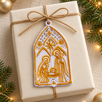 Lace nativity ornament tied with twine onto a cream wrapped Christmas gift beside evergreen branches.