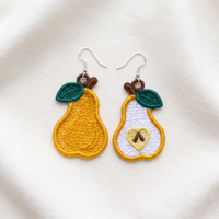 Whole and sliced pear FSL earrings with green leaves, brown stems and silver hooks on soft cream fabric