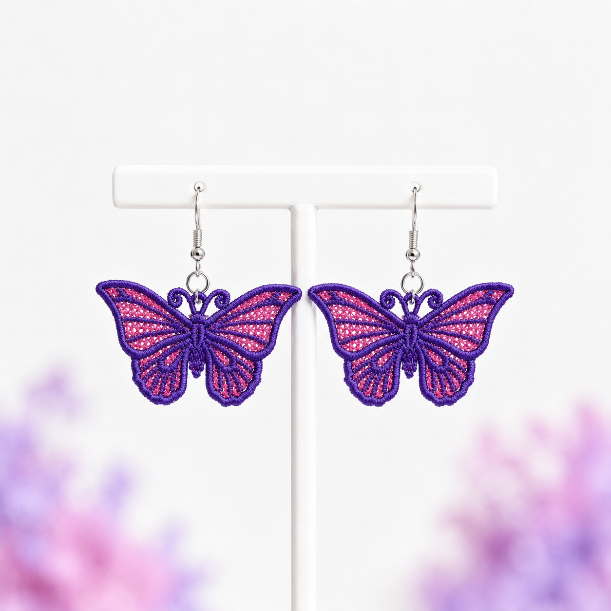 Pair of purple and pink butterfly FSL earrings with silver hooks displayed on a white jewelry stand