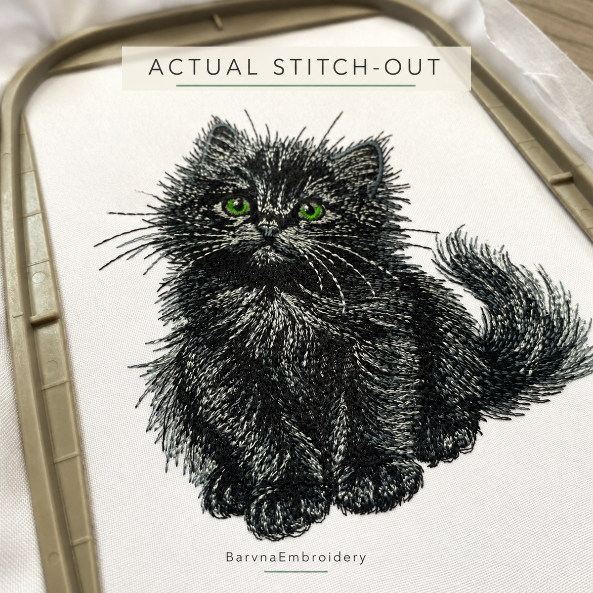 Close-up of an actual black kitten stitch-out on white fabric, showing textured fur, green eyes and fine whiskers.