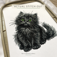 Close-up of an actual black kitten stitch-out on white fabric, showing textured fur, green eyes and fine whiskers.