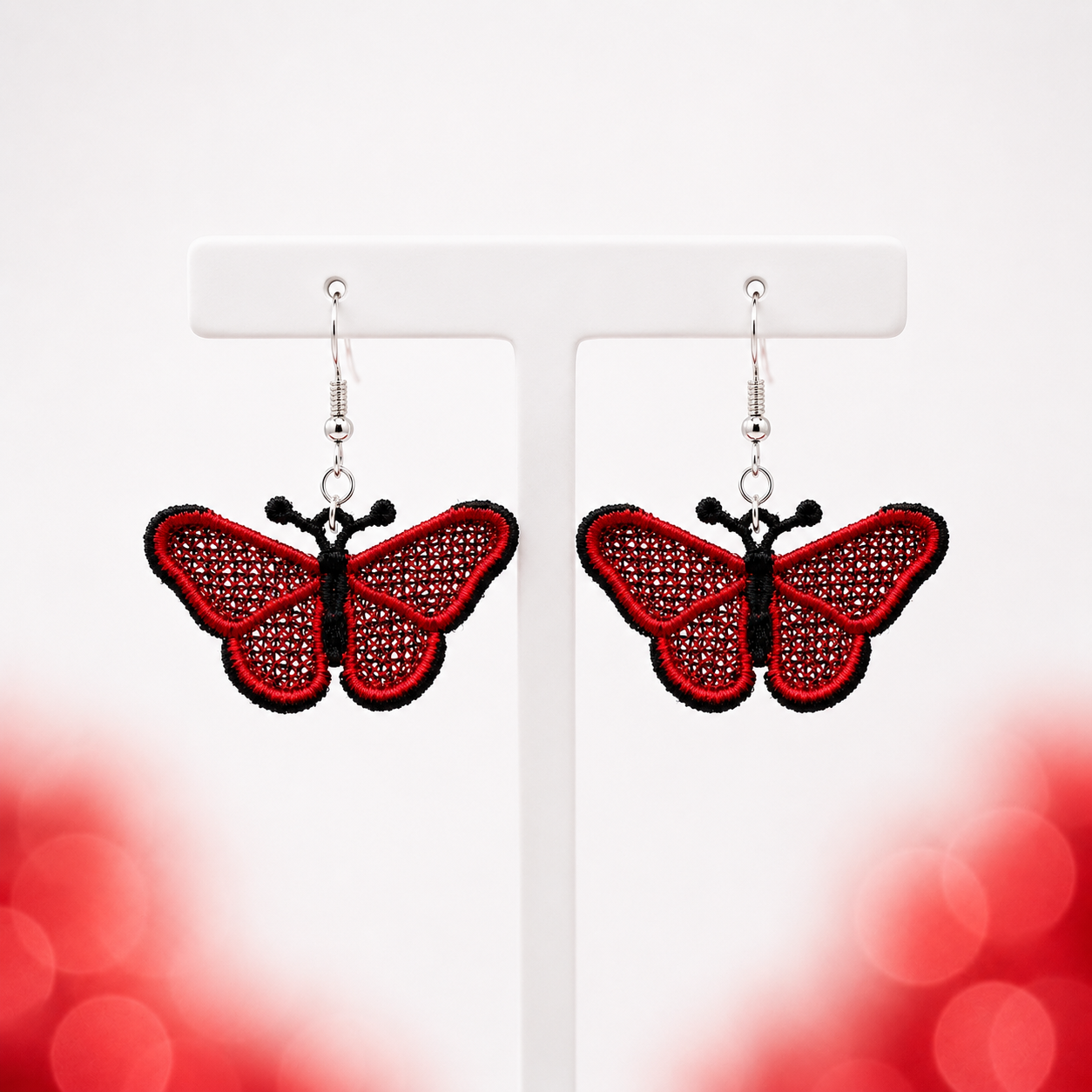 Pair of red and black butterfly FSL earrings with silver hooks displayed on a white jewelry stand