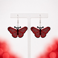 Pair of red and black butterfly FSL earrings with silver hooks displayed on a white jewelry stand