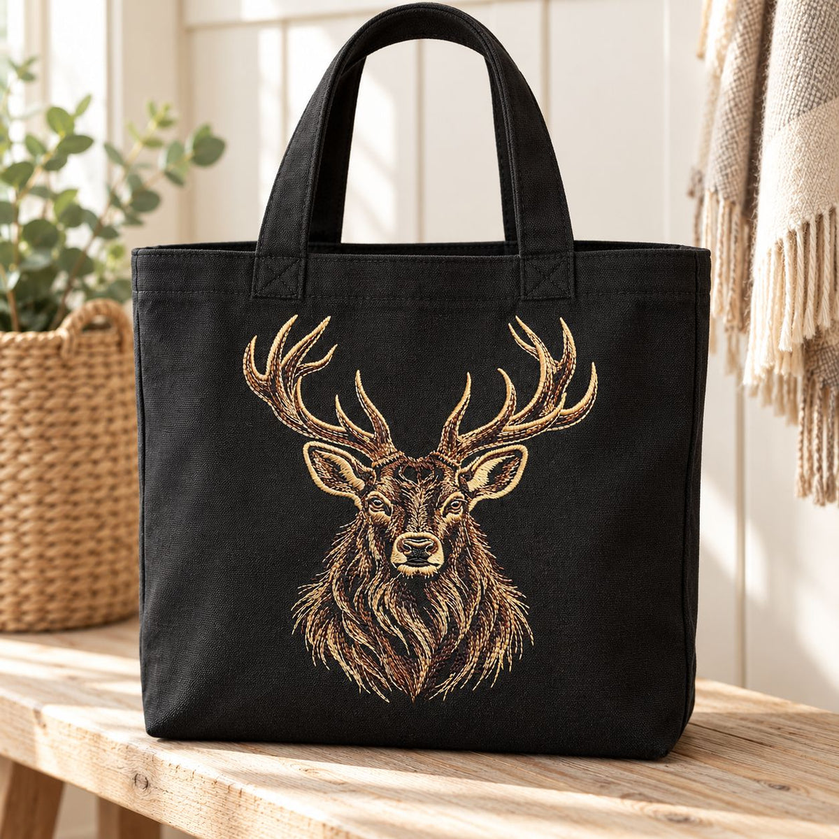 Black canvas tote bag mockup featuring an embroidered stag portrait with wide antlers and flowing neck fur.