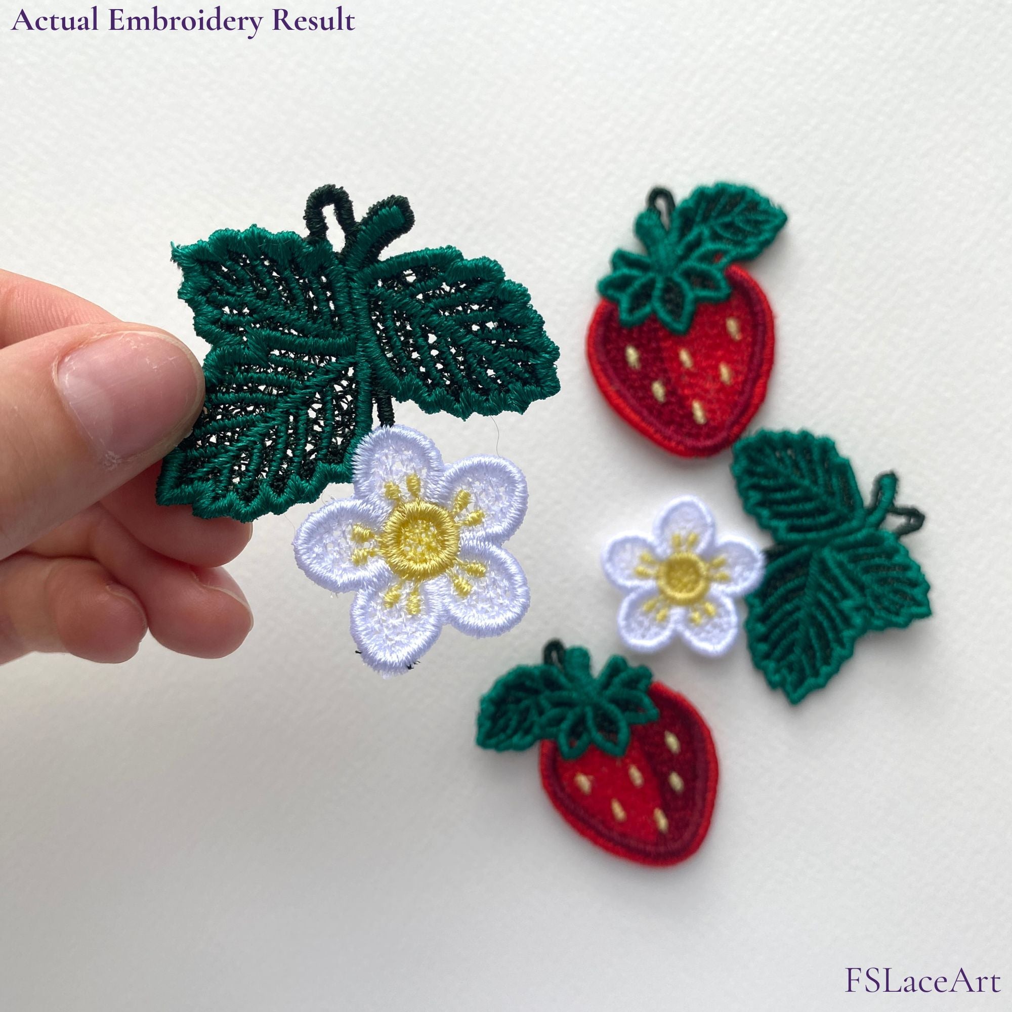 Hand holding an actual strawberry blossom FSL stitch-out with berry and flower designs in the background