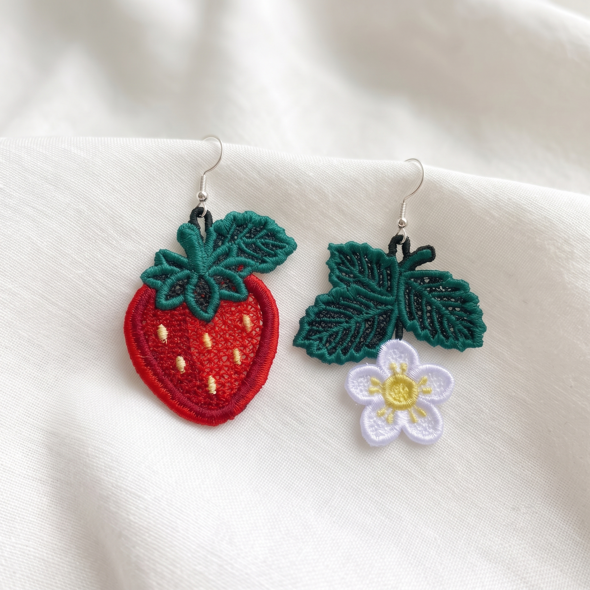 Red strawberry and white strawberry blossom FSL earrings with green leaves and silver hooks on soft white fabric