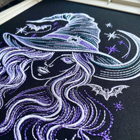 Close-up of witch embroidery on dark fabric showing satin outlines, purple hair details and crescent moon stitching.
